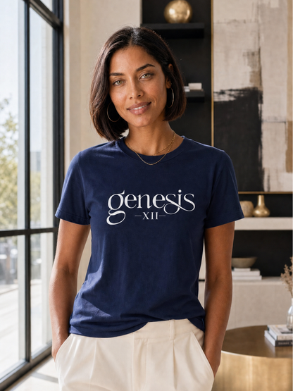 A woman wearing a navy blue t-shirt with 'genesis -XII-' printed in white script across the chest, paired with cream-colored pants, standing in a modern interior setting.